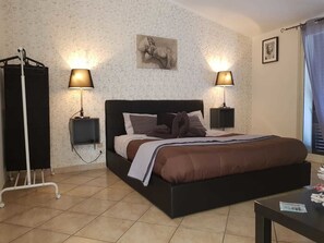 Un dormitorio con una cama grande, dos lámparas de noche, un cuadro en la pared y una ventana con cortinas.
