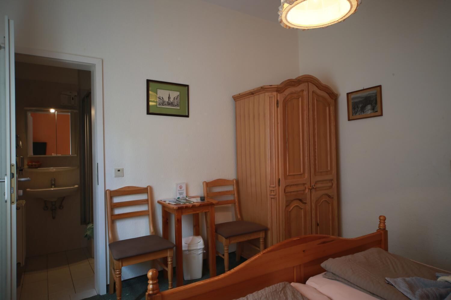 Un dormitorio con una cama, dos sillas de madera, una mesita, un armario y un espejo.