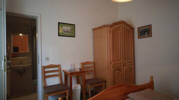 Un dormitorio con una cama, dos sillas de madera, una mesita, un armario y un espejo.