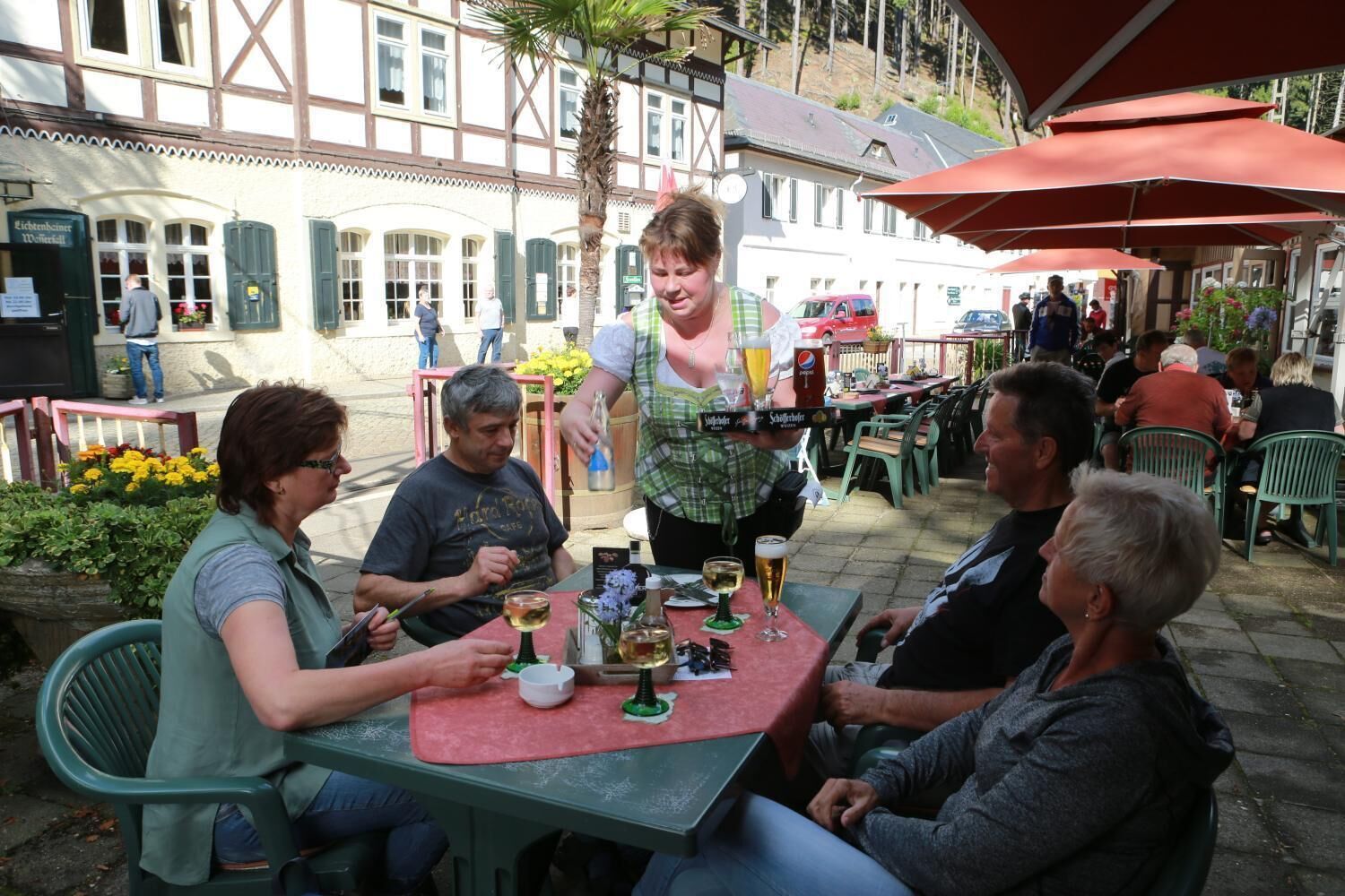 A group of people seated at an outdoor table with drinks, in a courtyard with buildings in the background.