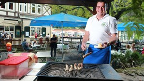 A man grilling sausages at an outdoor event with tables and umbrellas in the background. - Gaststätte & Pension Lichtenhainer Wasserfall (Sebnitz)