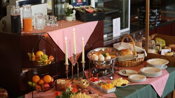 A buffet setup with various food items, including fruits, eggs, and bread, on a pink tablecloth. - Gaststätte & Pension Lichtenhainer Wasserfall (Sebnitz)