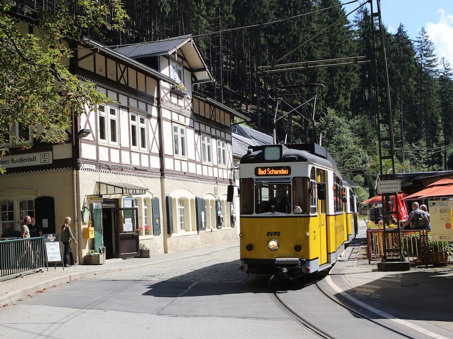 En gul og hvid sporvogn med teksten "Rad Schandau" foran, der kører forbi en bygning med et skilt "Viehhandel Schandau".
