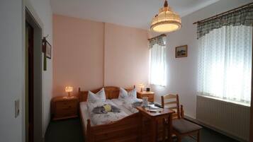 Ein Schlafzimmer mit einem hölzernen Bett, zwei Nachttischen mit Lampen, einem Sessel und einem Fenster mit Vorhängen.
