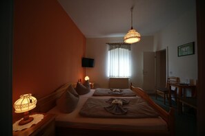 Un dormitorio con dos camas, televisión, ventana con cortinas y un área de comedor con sillas.