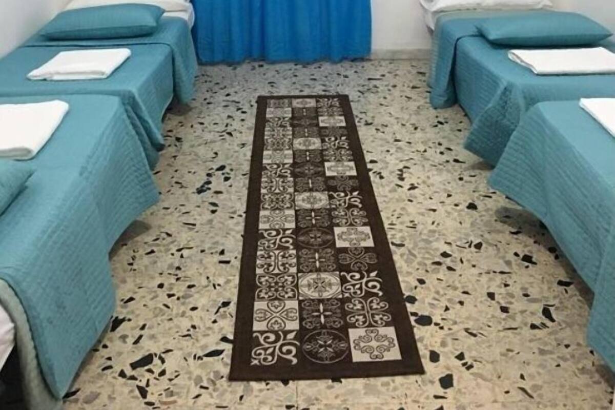 A room with two single beds, a blue curtain, a patterned rug, and two framed pictures on the walls.