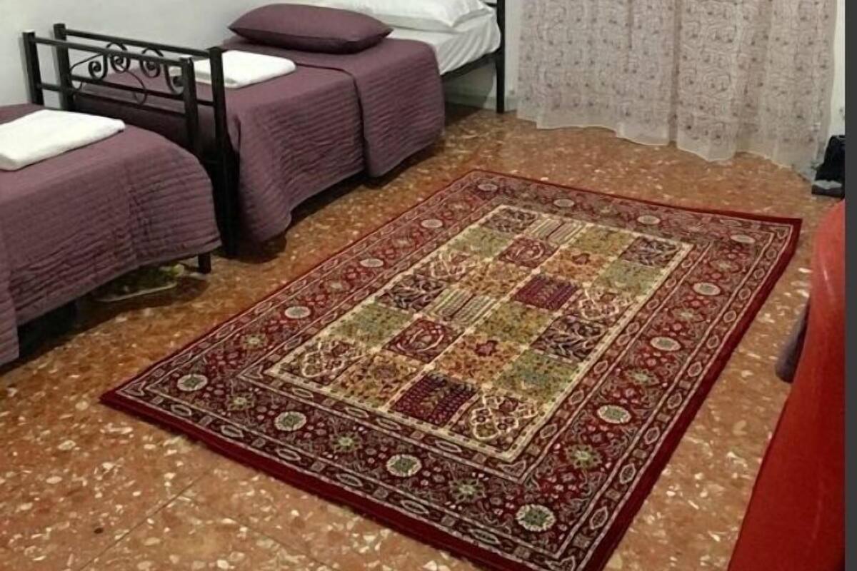 A small, simple room with two beds, a patterned rug, and a single wall picture.