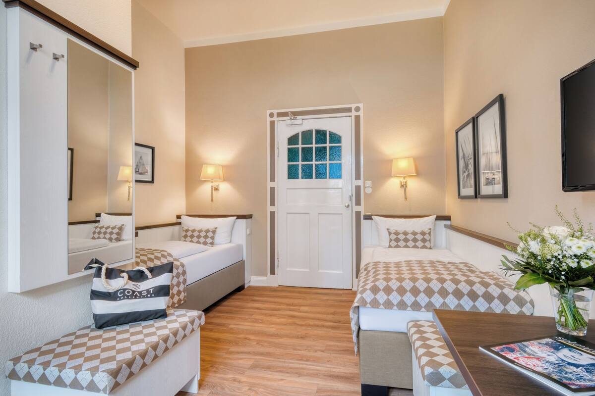 Habitación de hotel con dos camas, suelo de madera, puerta blanca y un televisor en la pared.