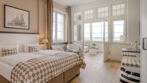 Une chambre d’hôtel avec un grand lit, un bureau, une chaise et une vue sur la mer grâce à de grandes fenêtres.
