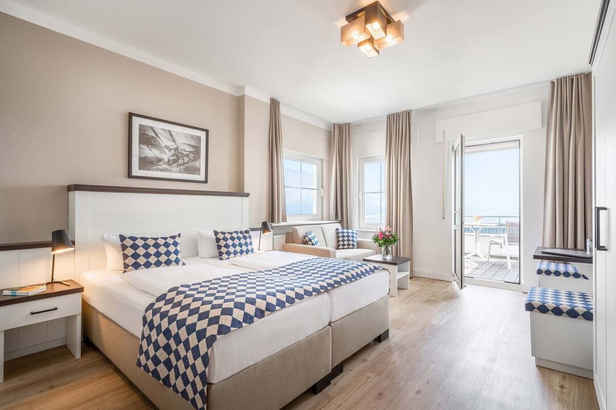 Habitación de hotel con una cama grande, una mesita de noche, un escritorio, una silla, un balcón con vistas y una lámpara de techo.