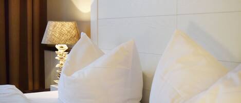 A hotel room with a neatly made bed, a lamp, and a wall-mounted shelf.