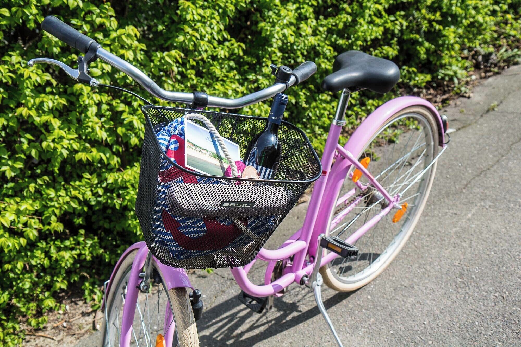 A pink bicycle with a basket containing a bottle, a bag, and a photo.