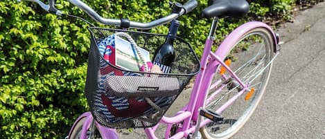 A pink bicycle with a basket containing a bottle, a bag, and a photo.