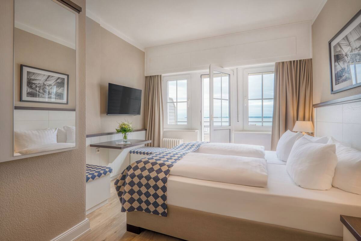 Una habitación de hotel con una cama grande, un televisor en la pared y una ventana con cortinas.