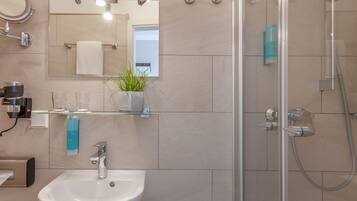 A modern bathroom with a glass shower enclosure, a sink with a mirror above it, and a potted plant on the countertop.