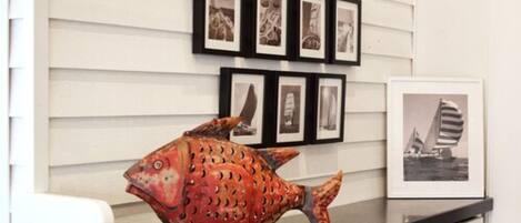 A fish sculpture on a counter with framed pictures on the wall behind it.
