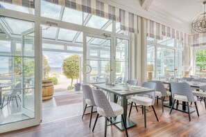 A dining area with glass doors leading to an outdoor patio, wooden flooring, and patterned chairs. - Strandschlösschen (Lübeck)
