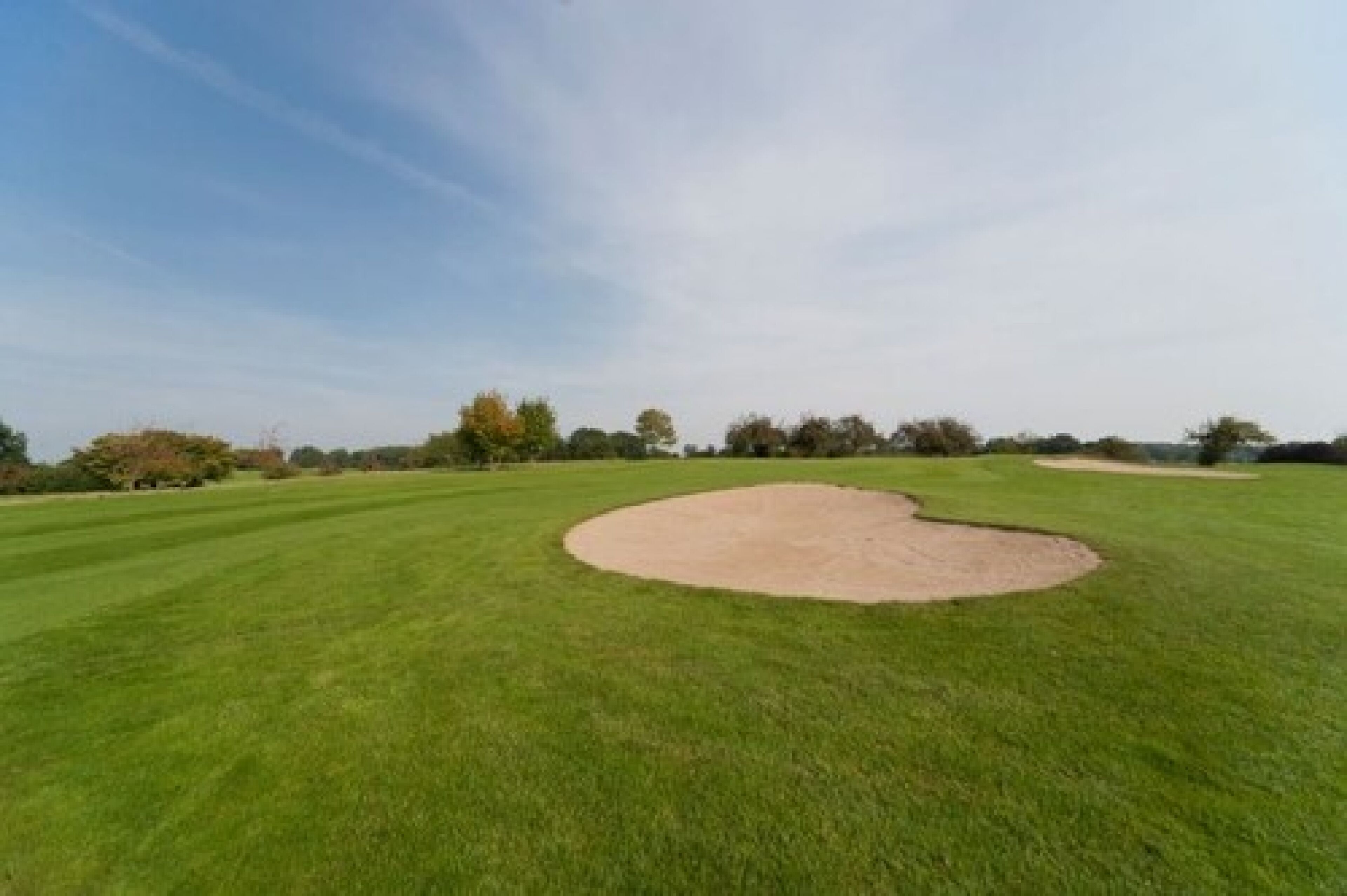Un campo de golf con un green impecable, búnkeres de arena y árboles al fondo.