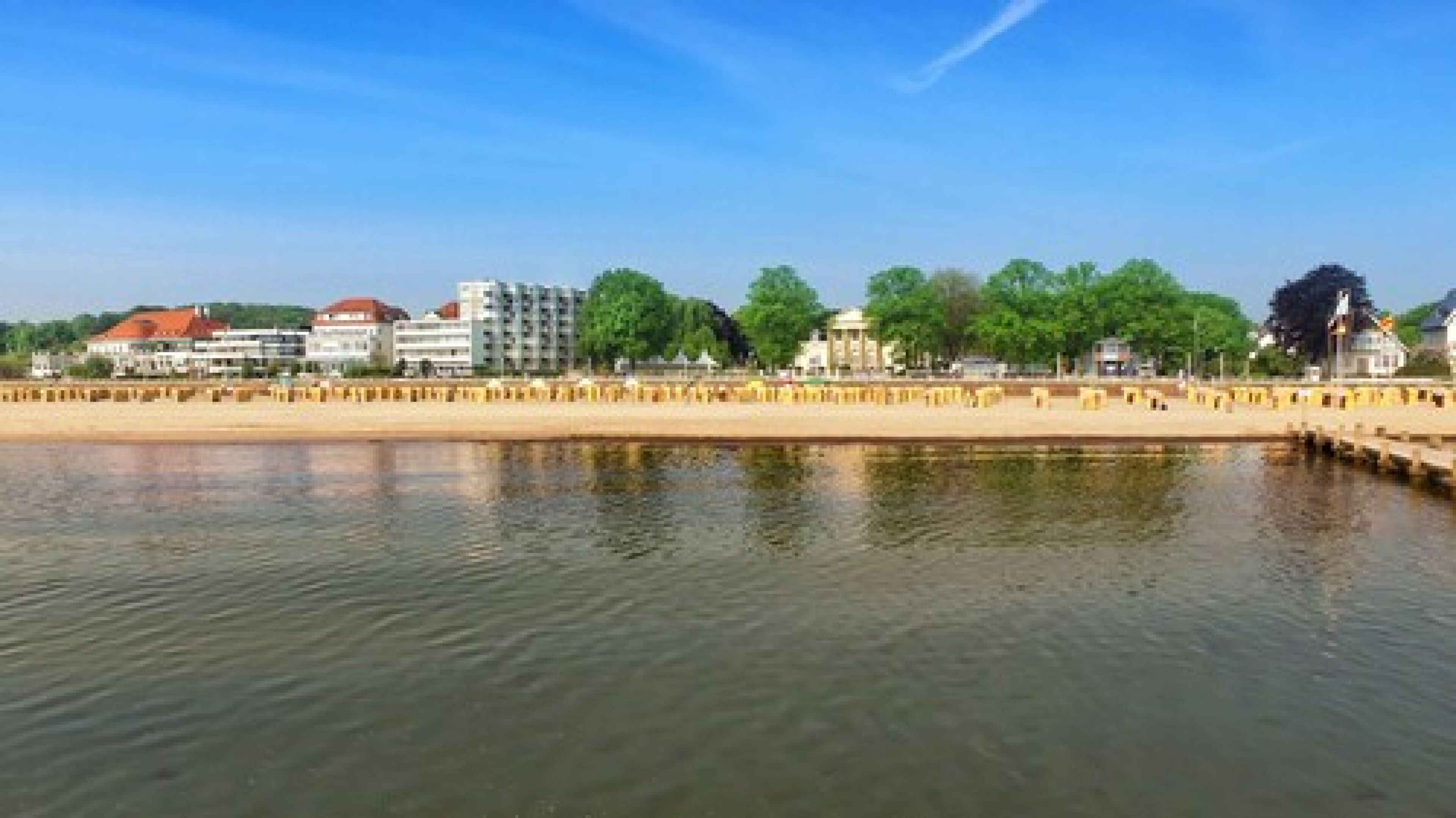 Vista al agua con edificios, una playa de arena y una superficie acuática tranquila.