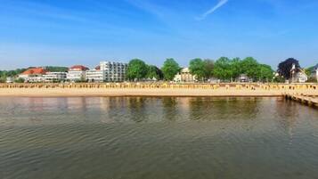 Vista al agua con edificios, una playa de arena y una superficie acuática tranquila.