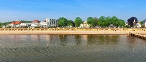 A waterfront view with buildings, a sandy beach, and a calm body of water.