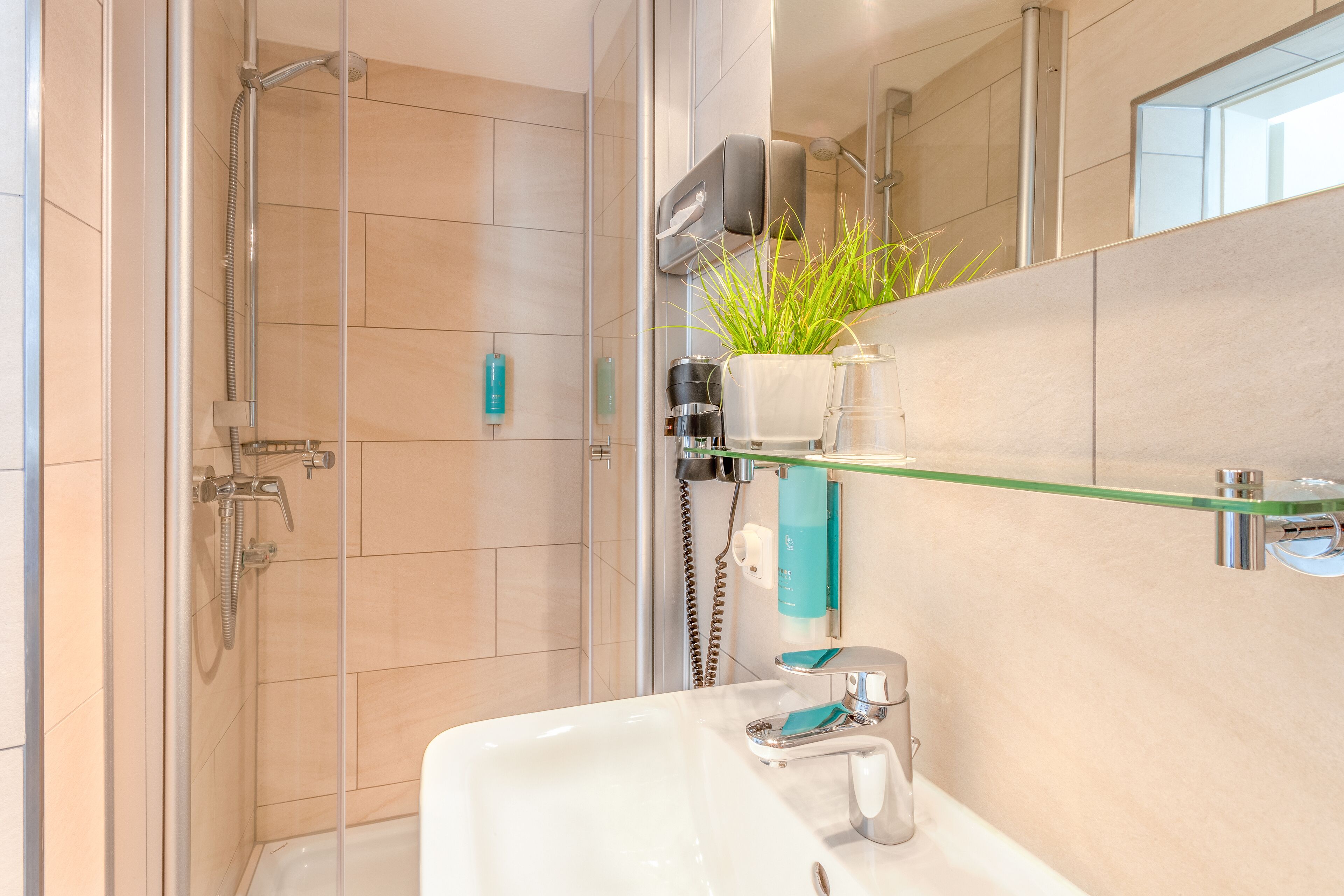 Ein modernes Badezimmer mit einer Duschkabine aus Glas, einem weißen Waschbecken und einem Spiegel darüber.
