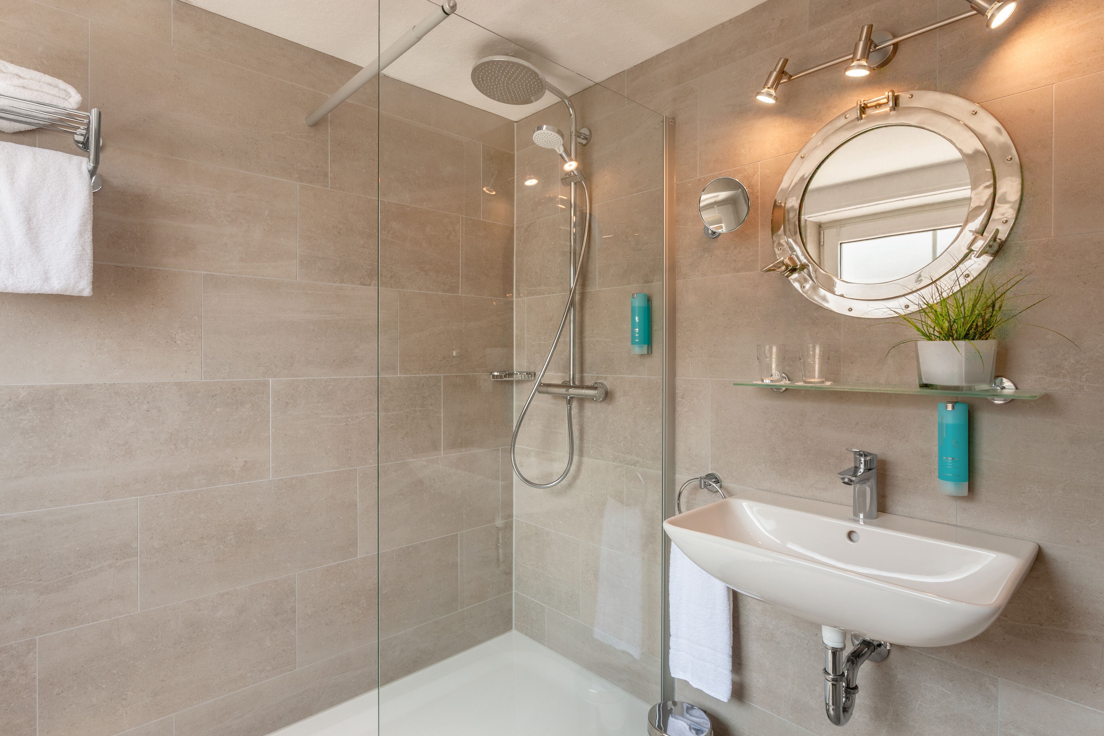 A modern bathroom with a glass-enclosed shower, a white sink, and a round mirror.
