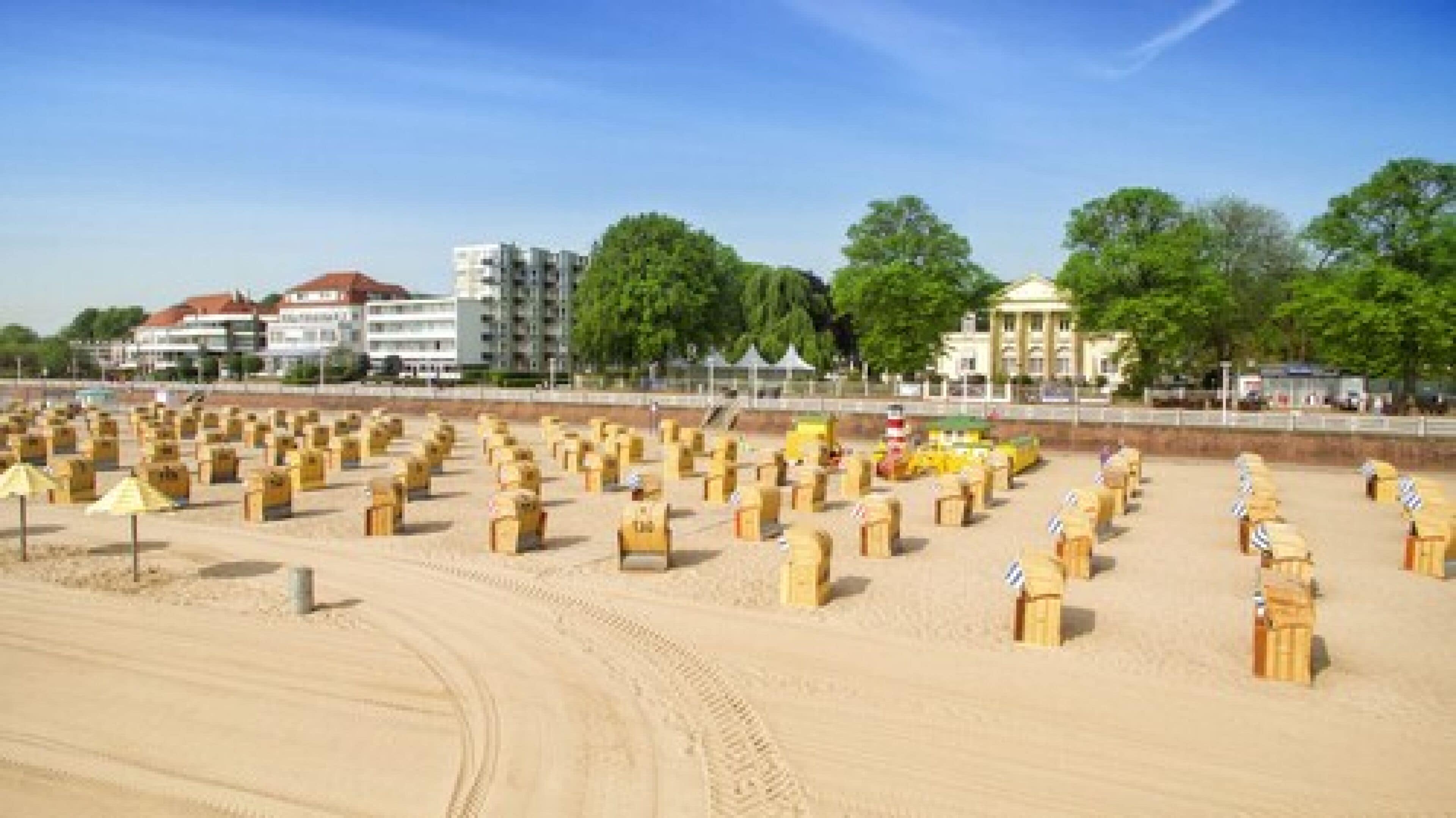 Une plage de sable bordée de rangées de structures en bois, probablement destinées à protéger du soleil, et des bâtiments visibles à l’arrière-plan.