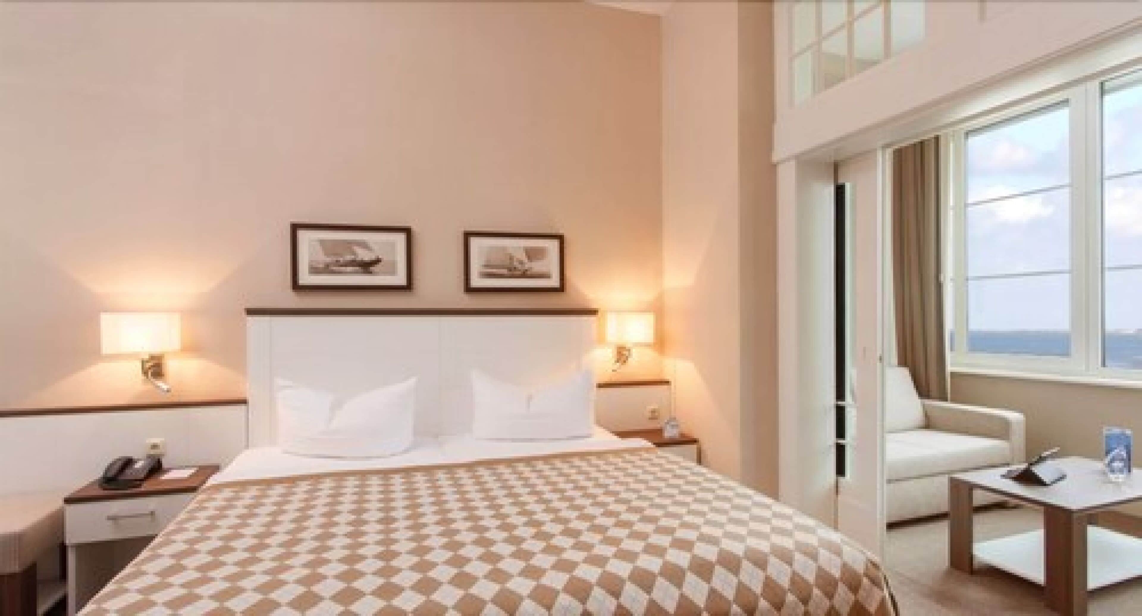 A hotel room with a large bed, two bedside lamps, a chair, a small table, and a window with a view.