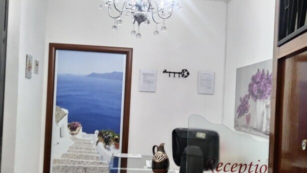 A reception area with a chandelier, a framed landscape painting, a reception desk, and a door leading to a staircase. - A Casa Carmen (Aversa)