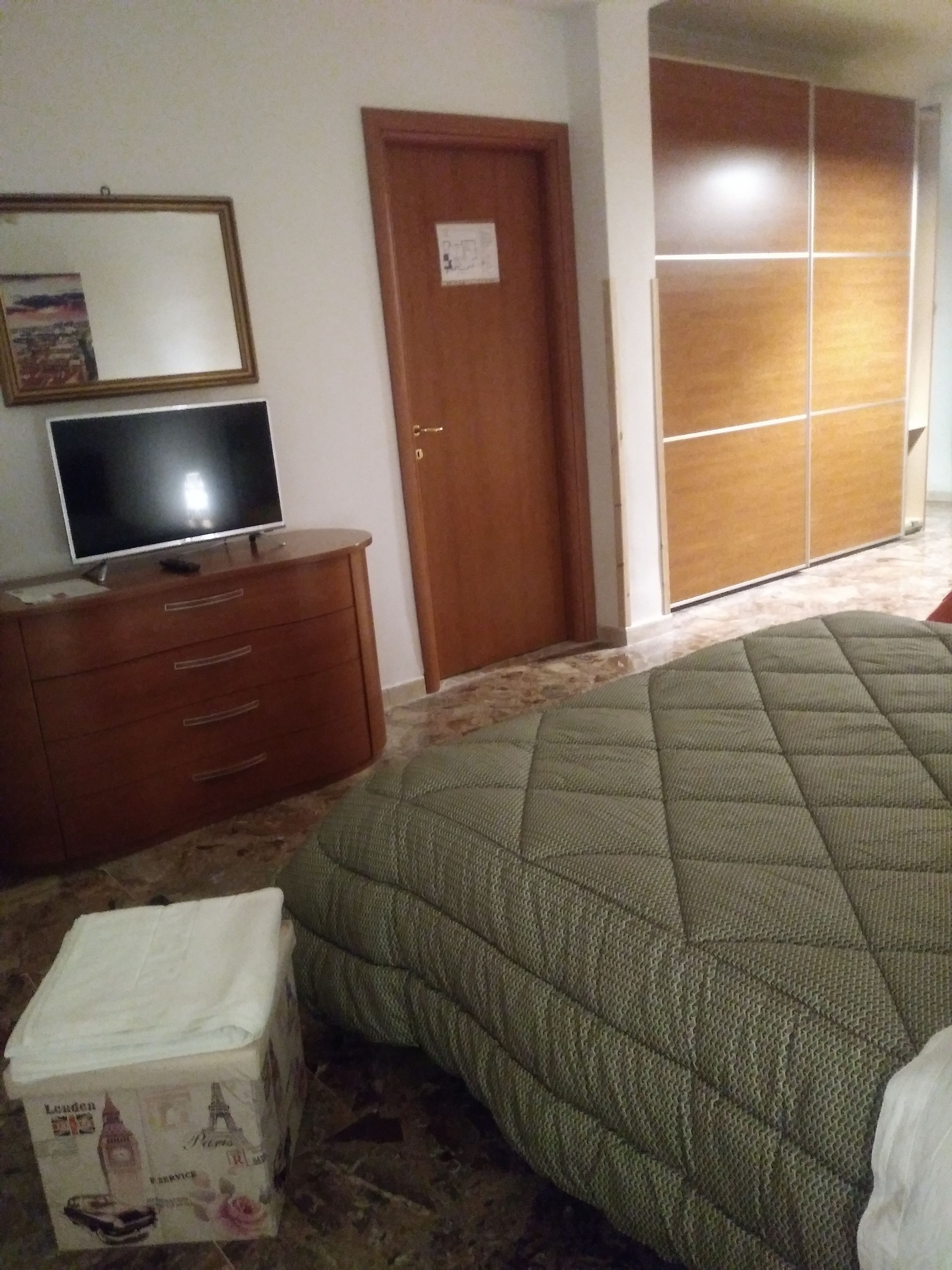 A bedroom with a bed, a wooden dresser, a television, and a wardrobe.