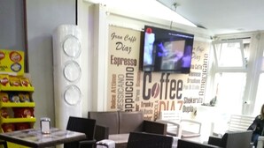 A cafe interior with tables and chairs, a wall-mounted TV, and a snack shelf. - A Casa Carmen (Aversa)