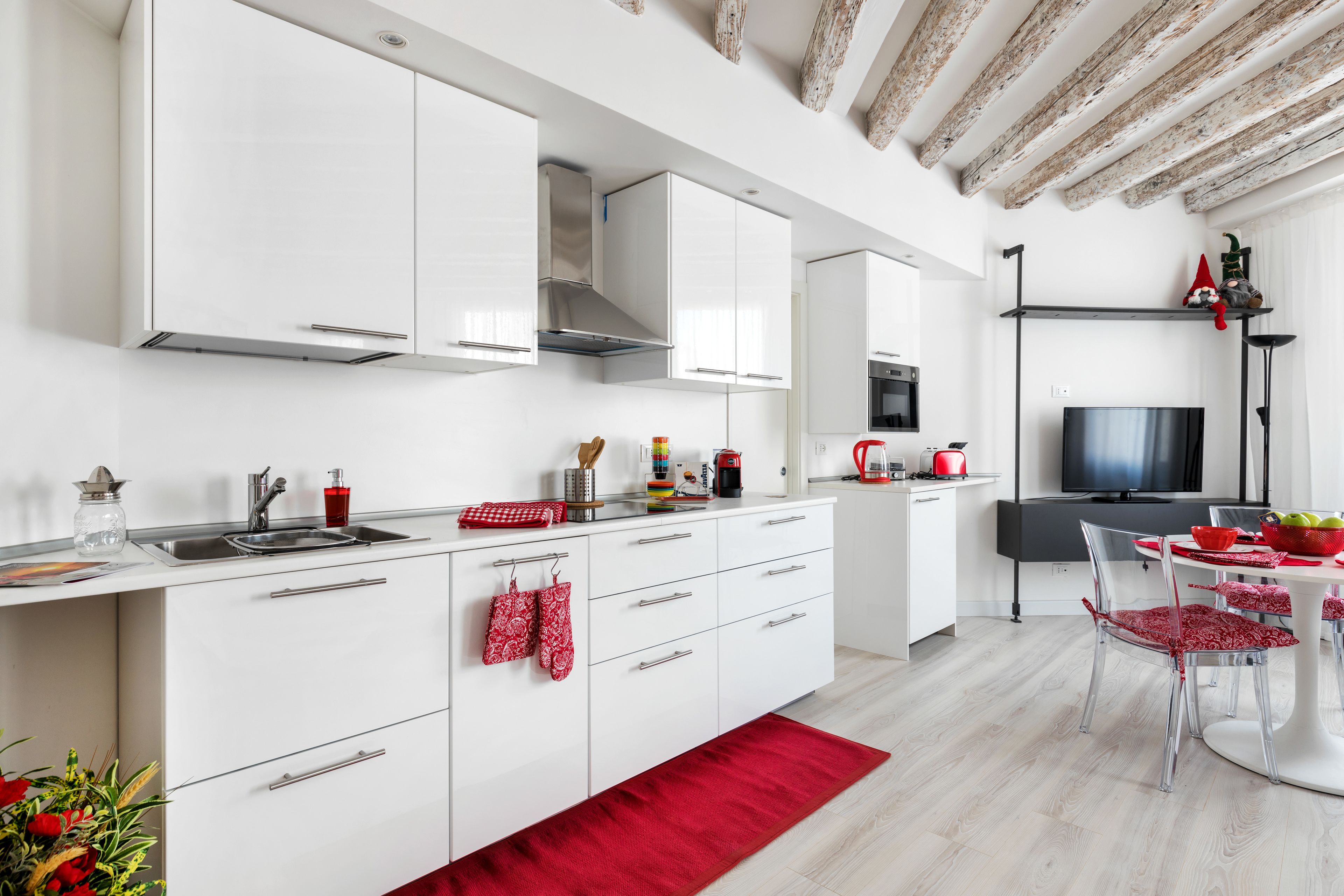 Una cucina moderna con mobili bianchi, una cappa in acciaio inossidabile e un tappeto rosso.
