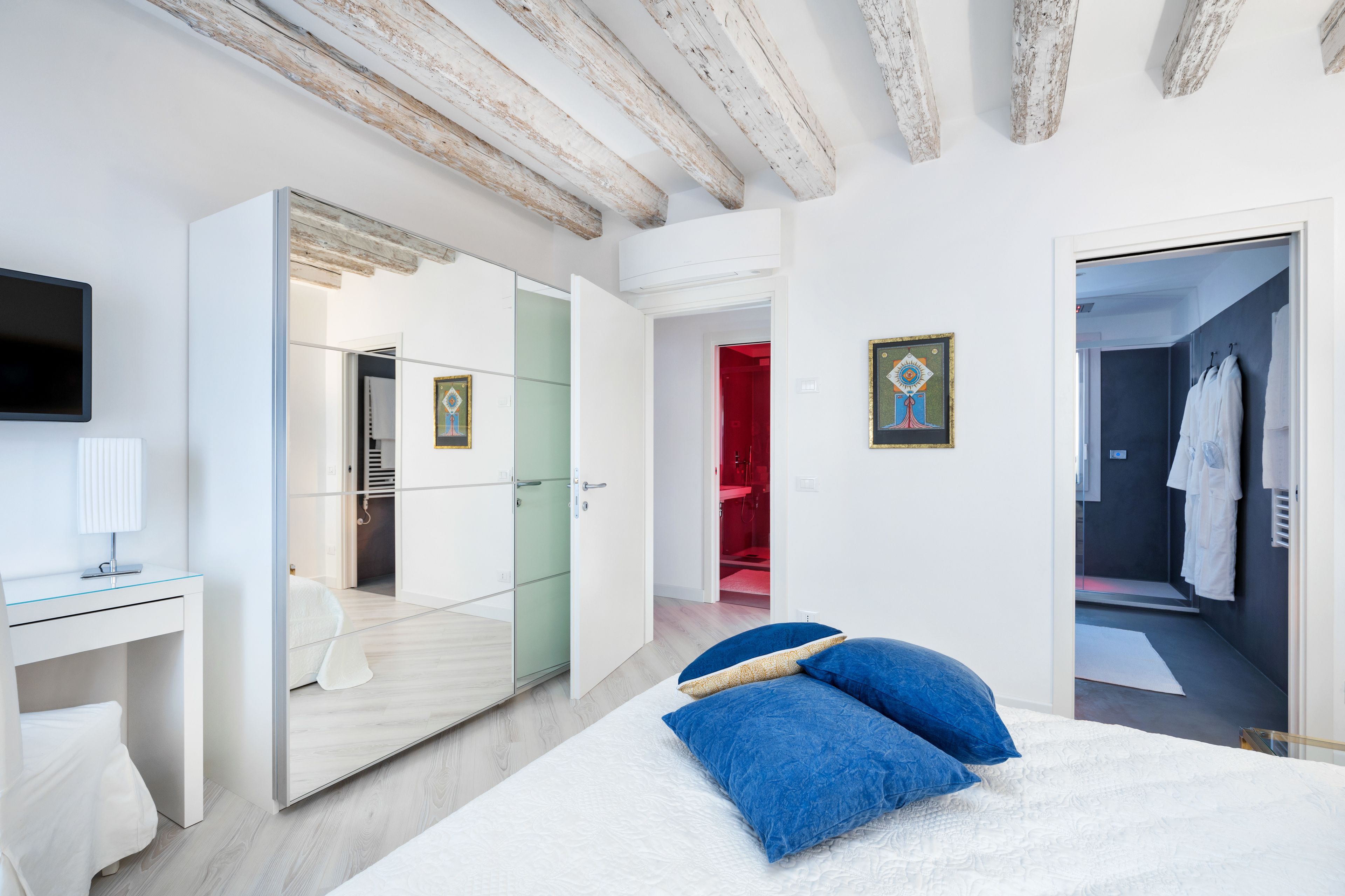 Un dormitorio moderno con cama, escritorio, televisor y vestidor.