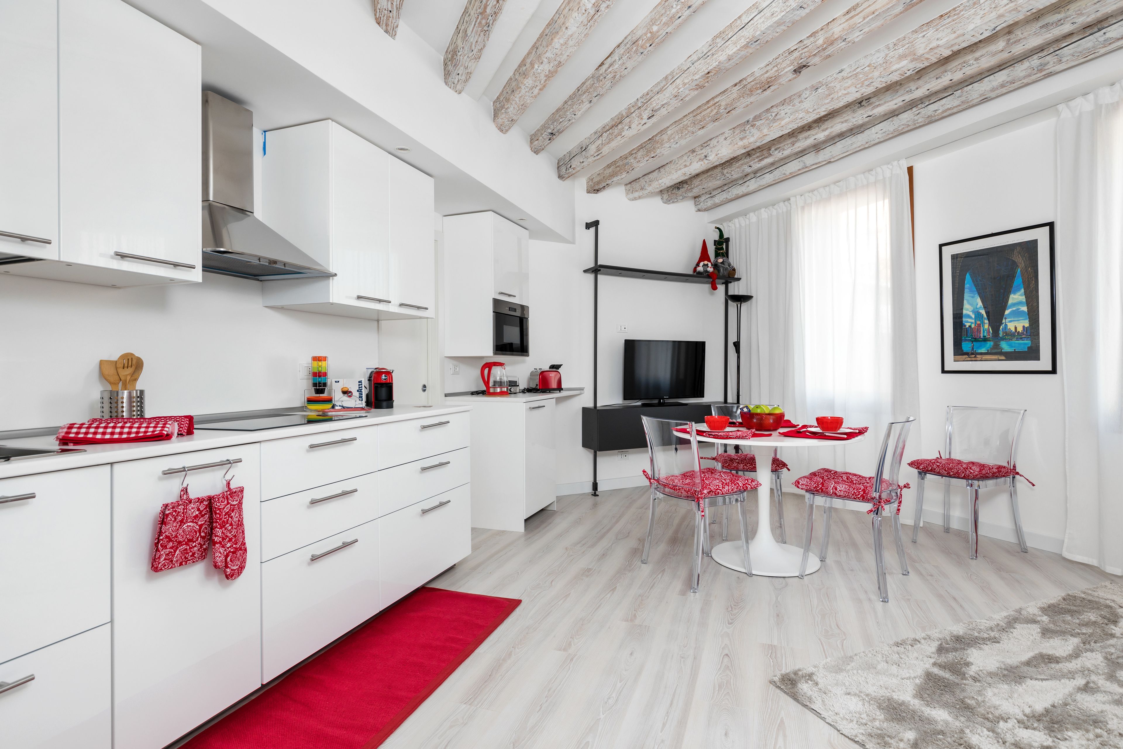Uma cozinha moderna com armários brancos, um exaustor de aço inoxidável e uma área de jantar com mesa e cadeiras brancas.