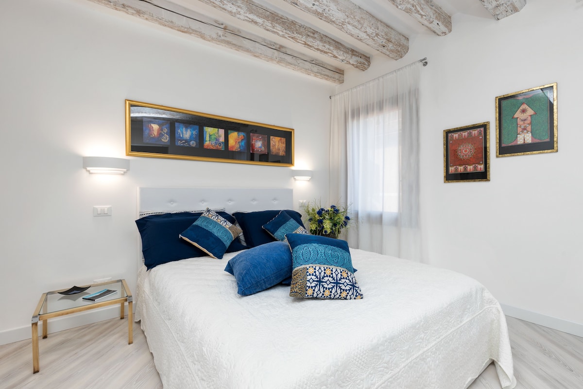 A bedroom with a bed, pillows, a bedside table, and framed artwork on the wall.