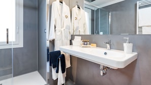Un baño moderno con un espejo grande, un lavabo blanco y dos albornoces blancos colgados en un perchero.