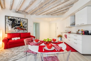 A modern living space with a red sofa, a glass dining table with red placemats, and a kitchen area with white cabinets. - Venice Heaven Apartments Biennale (Venice)