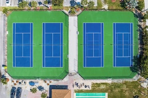 Vue aérienne d’un complexe de courts de tennis comprenant deux terrains, un parking et des espaces verts environnants.