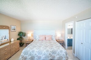 A bedroom with a bed, nightstands, a dresser, a plant, and a bathroom visible through an open door.