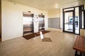 A lobby with two elevators, a mailbox area, and a wooden bench.