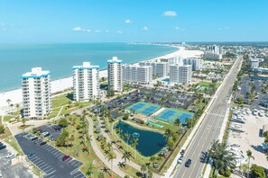 A coastal cityscape with high-rise buildings, a beach, and a parking lot with tennis courts.