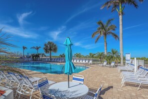 A pool area with lounge chairs and umbrellas, surrounded by palm trees.