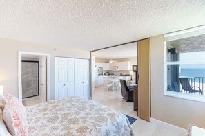 Ein Schlafzimmer mit Bett, ein Badezimmer mit Dusche und Blick auf einen Balkon mit Stühlen.
