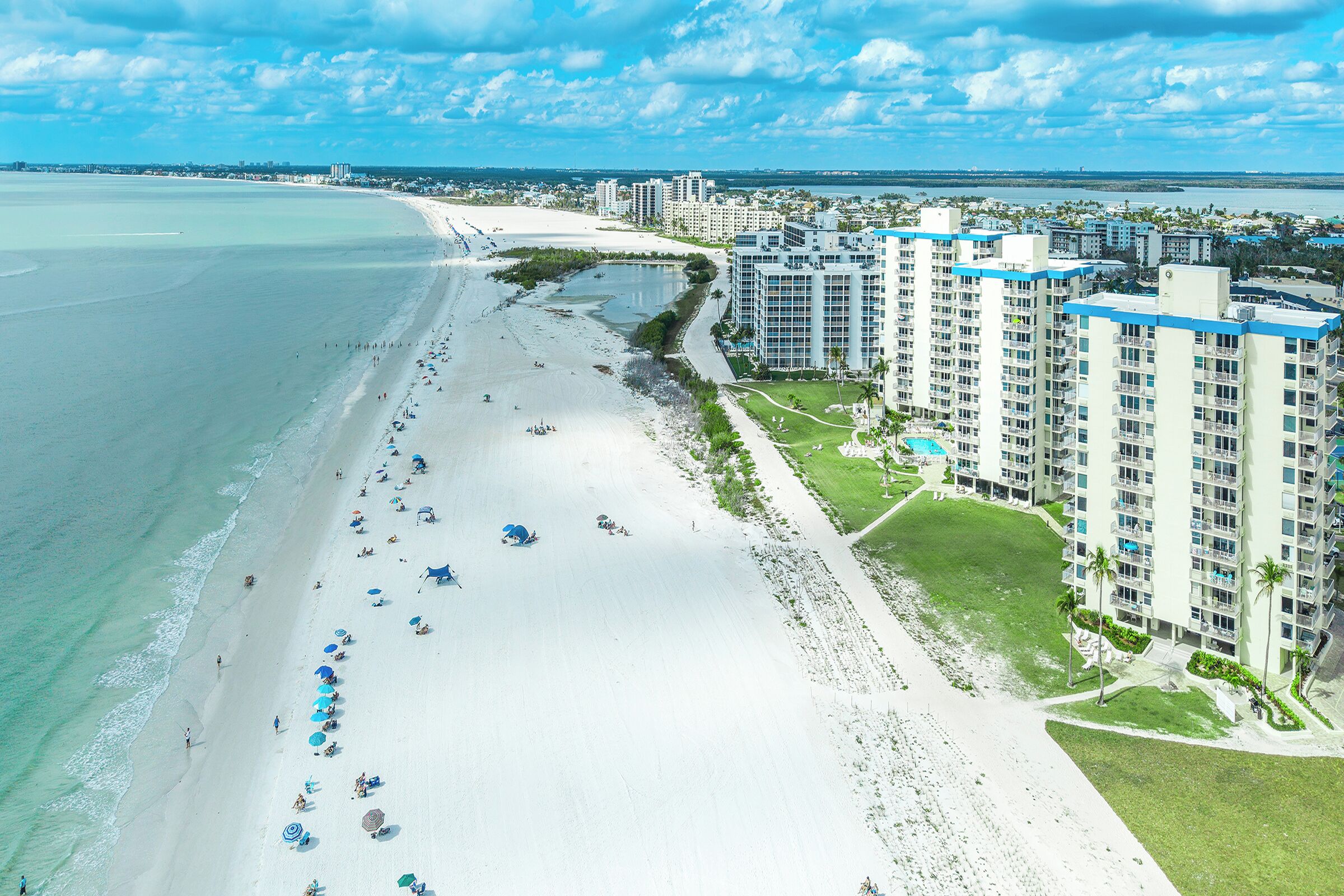 A coastal hotel with a beachfront view, multiple high-rise buildings, and a sandy beach with umbrellas.
