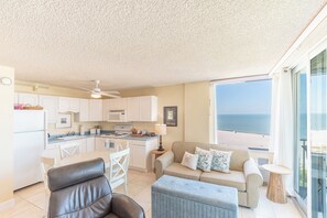 Une cuisine moderne avec des meubles blancs, un coin repas comprenant une table et des chaises, et une vue sur l’océan grâce à de grandes fenêtres.