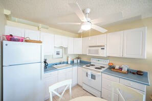 A compact kitchen with white cabinets, a stove, a microwave, a ceiling fan, and a refrigerator.