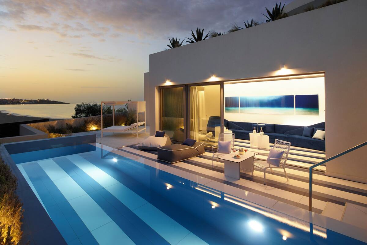 Un espace de vie extérieur moderne, doté d’une piscine, de coins salon et offrant une vue sur l’océan au crépuscule.