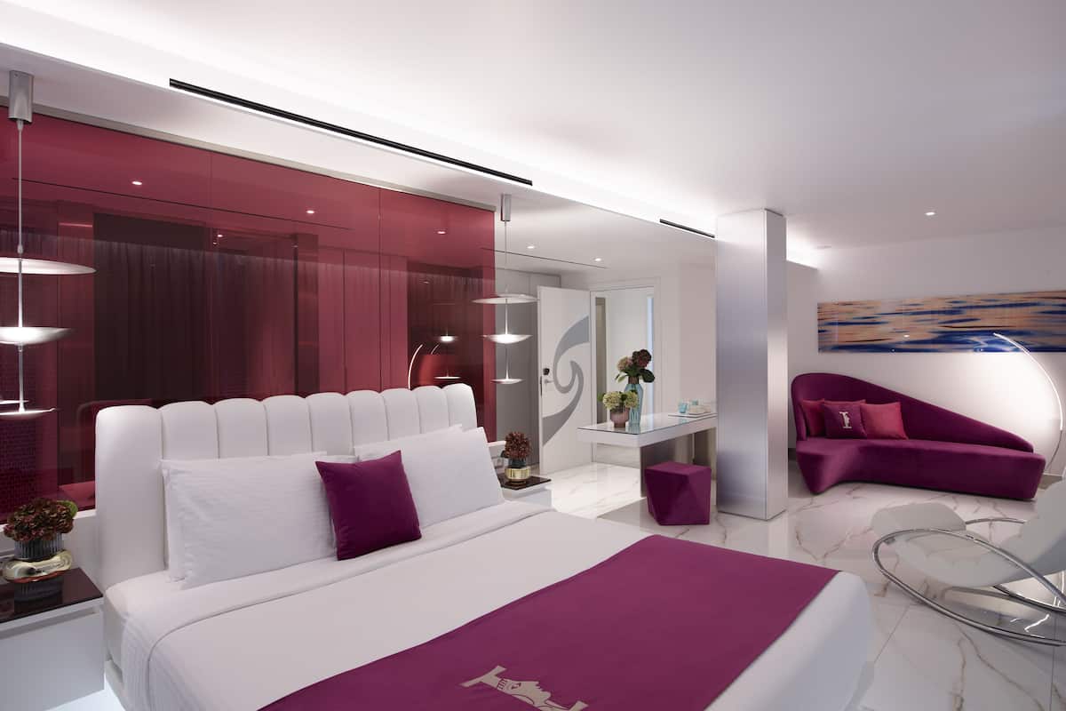 Une chambre moderne avec un grand lit, un bureau en verre et un canapé violet.