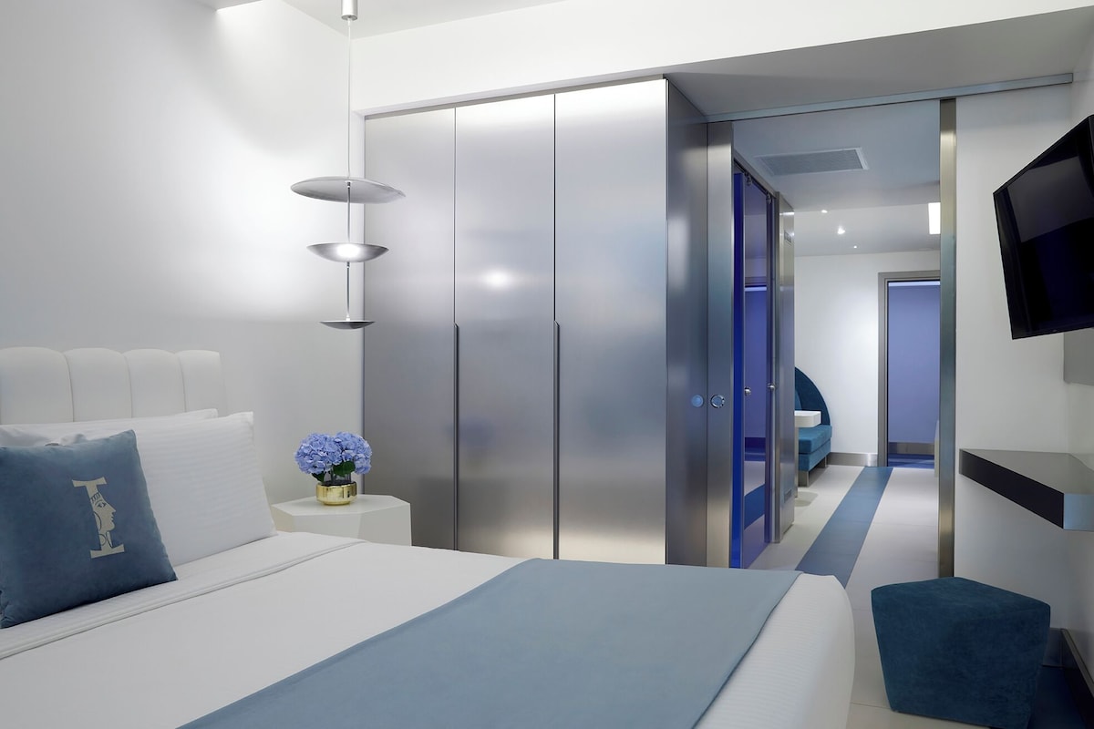 A modern hotel room with a bed, bedside tables, a wardrobe, and a TV mounted on the wall.